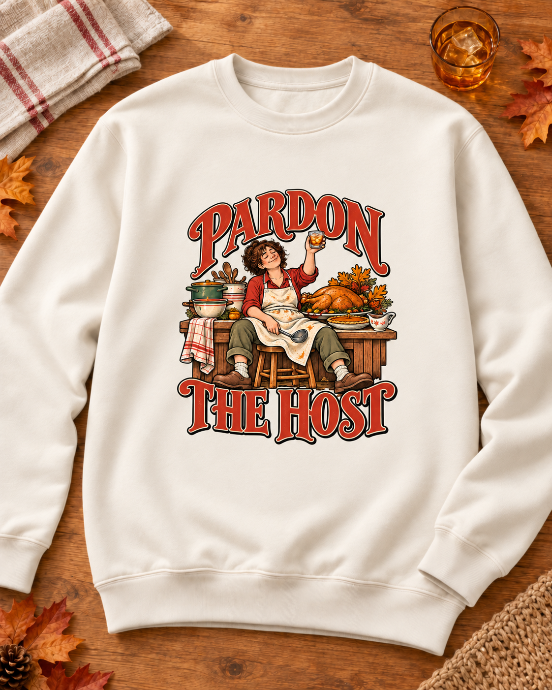 Pardon the Host raised-drink design on a Pigment Ivory crewneck sweatshirt, styled on warm kitchen wood