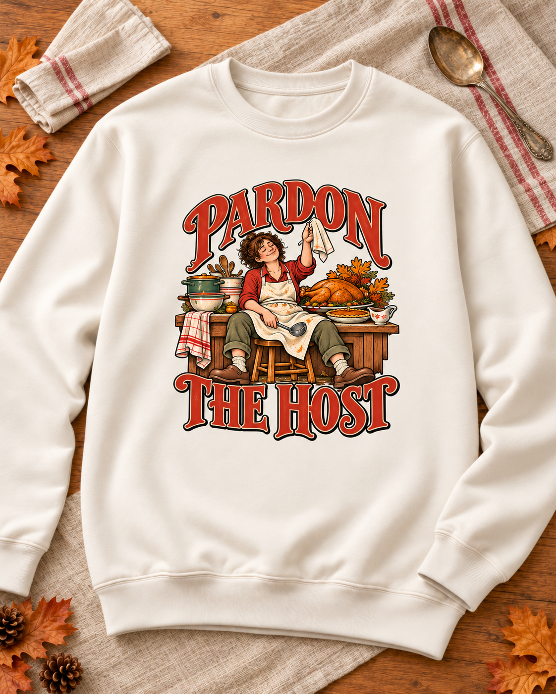Generated styling preview: Pardon the Host original towel design on a Pigment Ivory crewneck sweatshirt, styled with autumn leaves